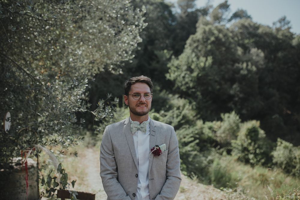 Groom in light gray suit standing in a sunny outdoor garden setting.