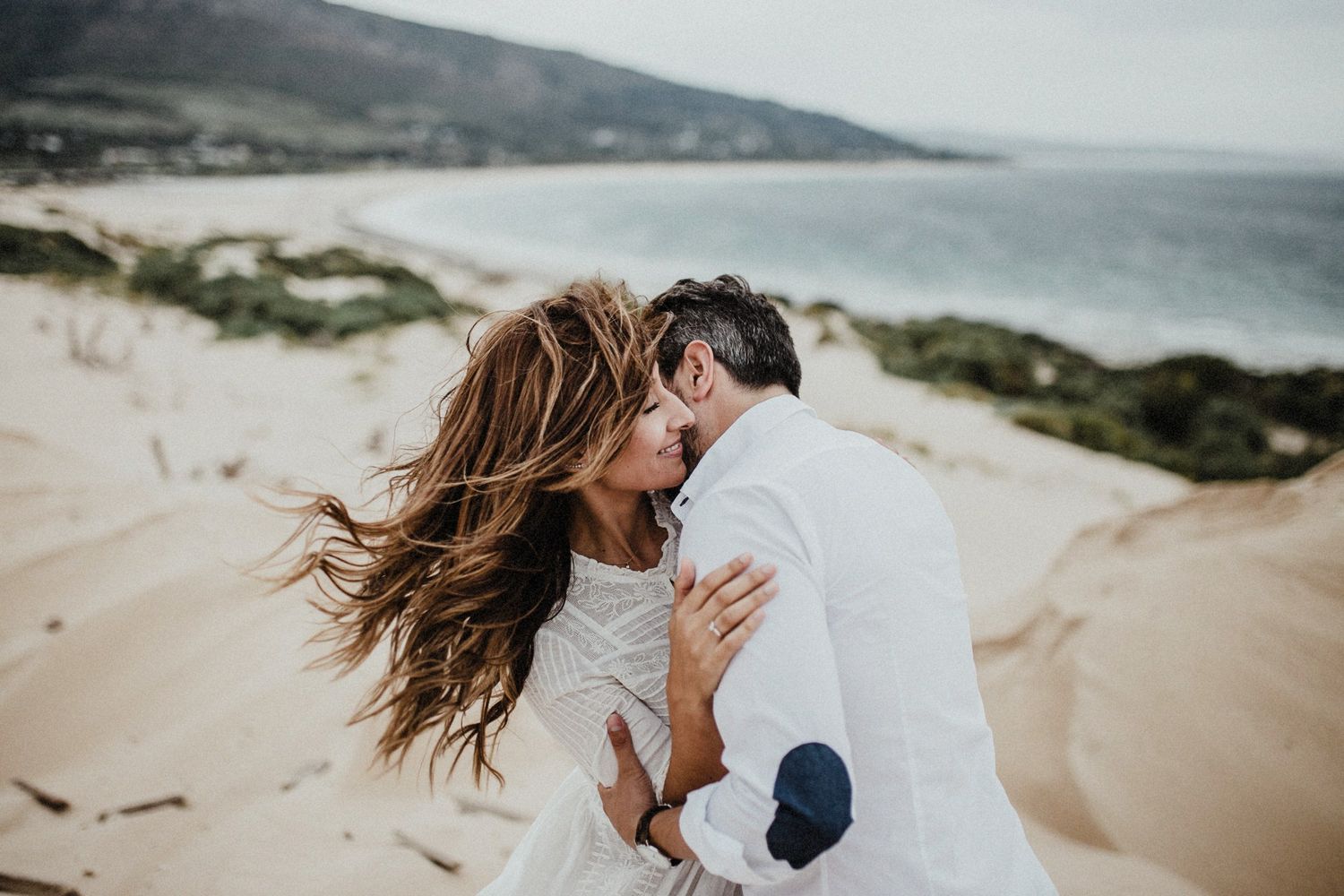 Wind-swept romantic moment between couple on sandy beach dunes.