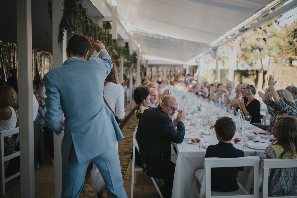 Wedding guests enjoy a celebration dinner at elegantly decorated reception tables with white linens and greenery decor.