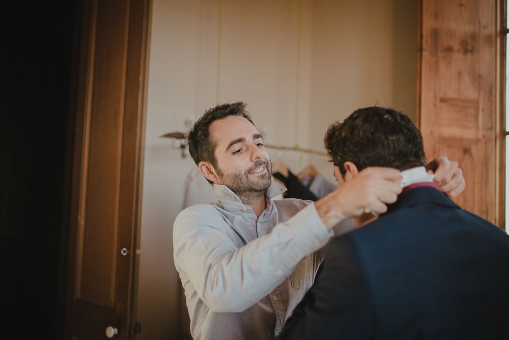 Two people helping each other get ready for a formal event in a warmly lit room.
