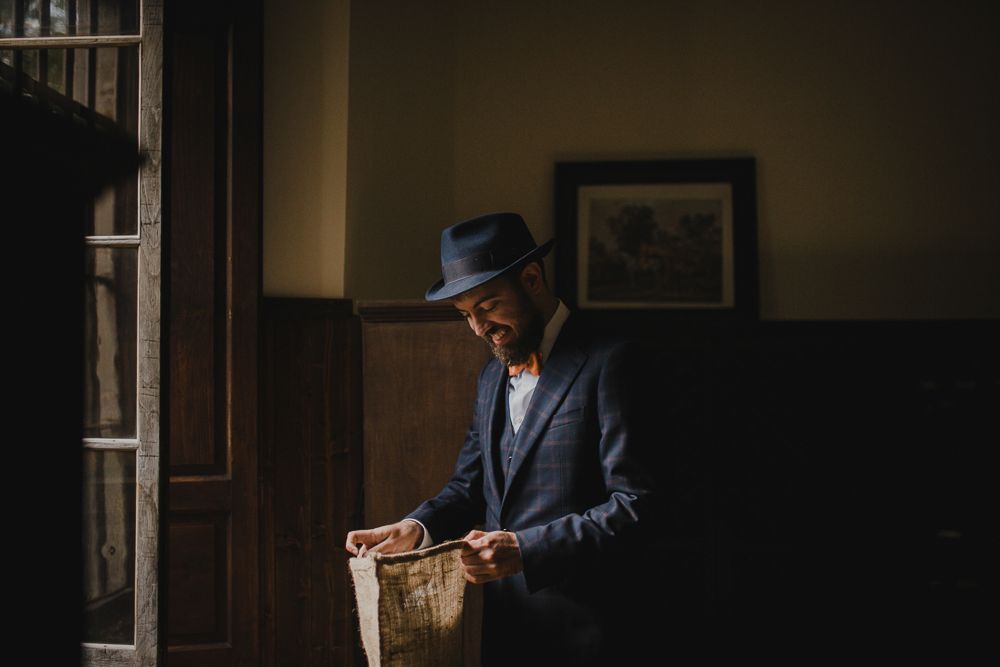 Figure in vintage attire and hat examining papers in shadowy interior.