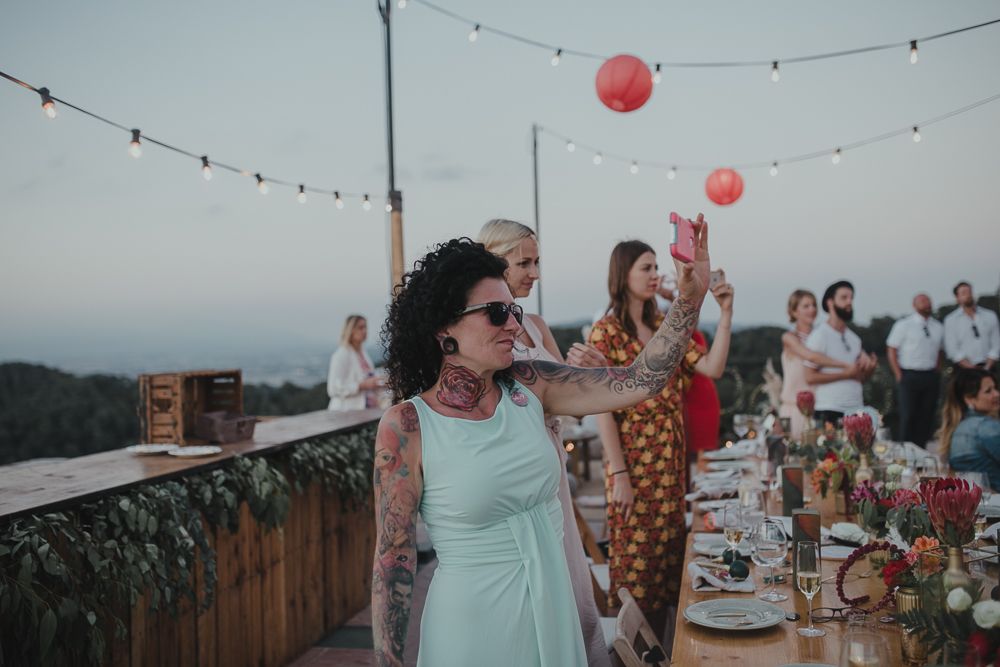 Outdoor wedding reception on mountain terrace with string lights and pink balloons at dusk.