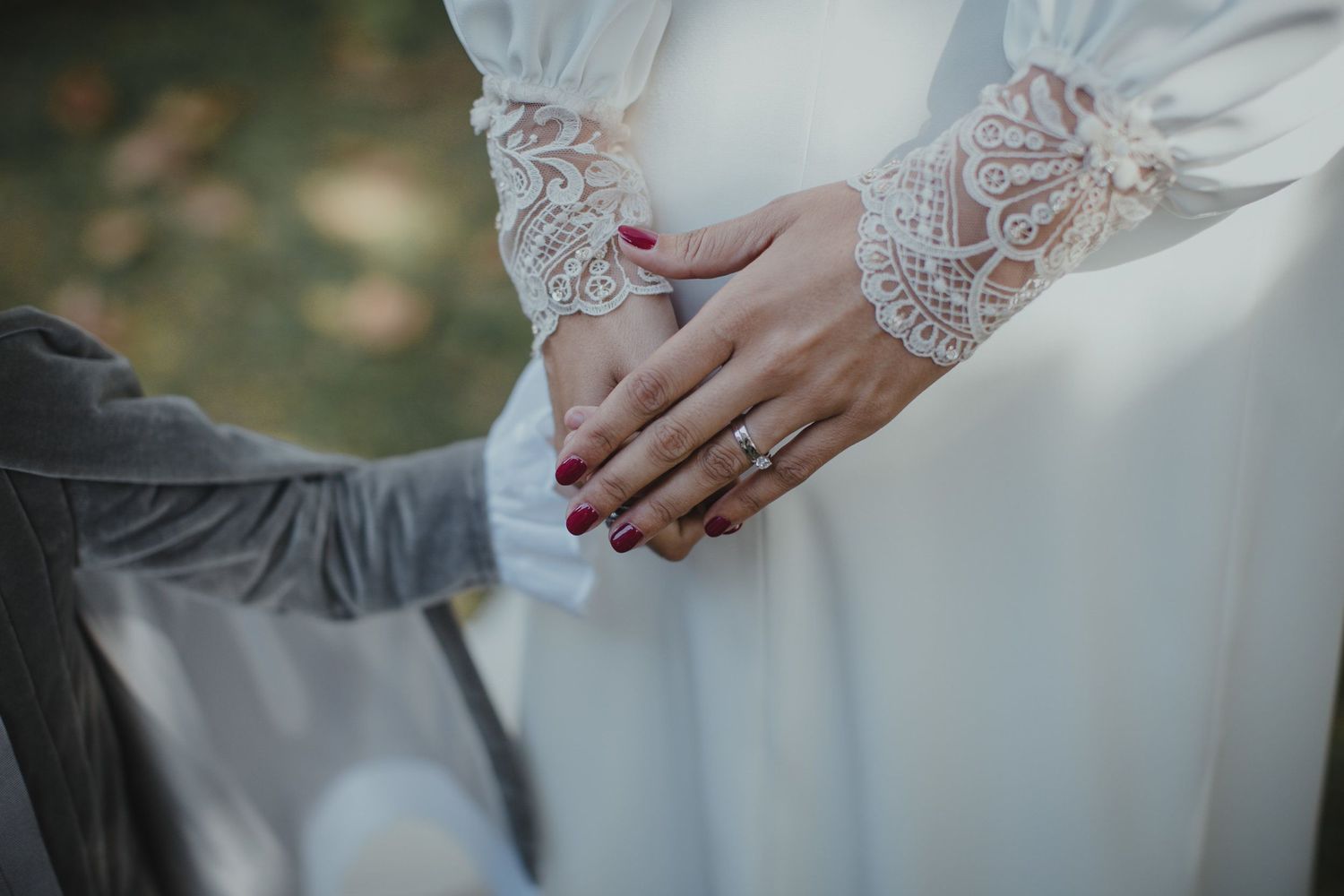 Detail shot of lace sleeve wedding dress with clasped hands showing elegant manicure.