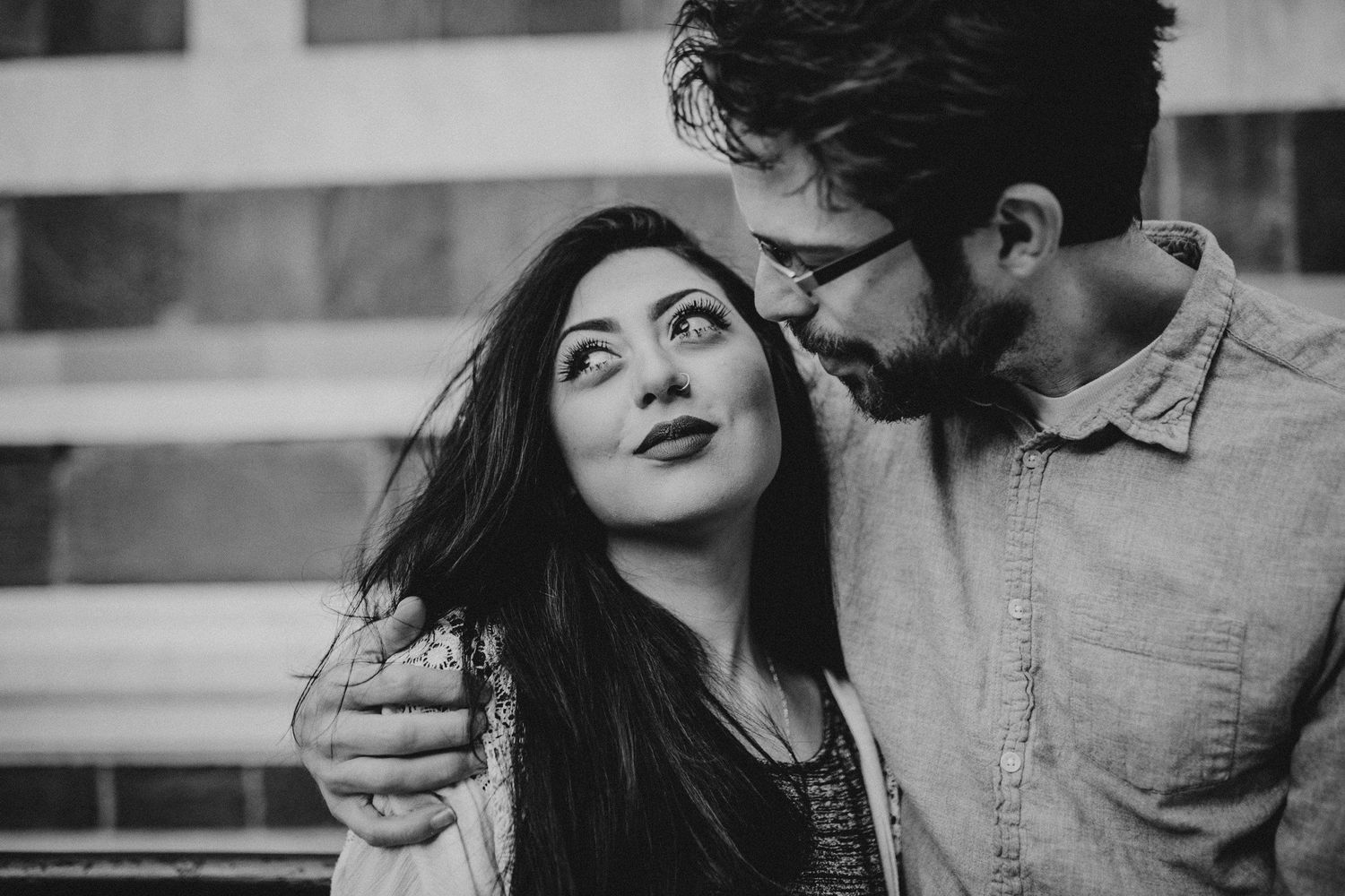 Intimate black and white portrait of couple against urban backdrop.