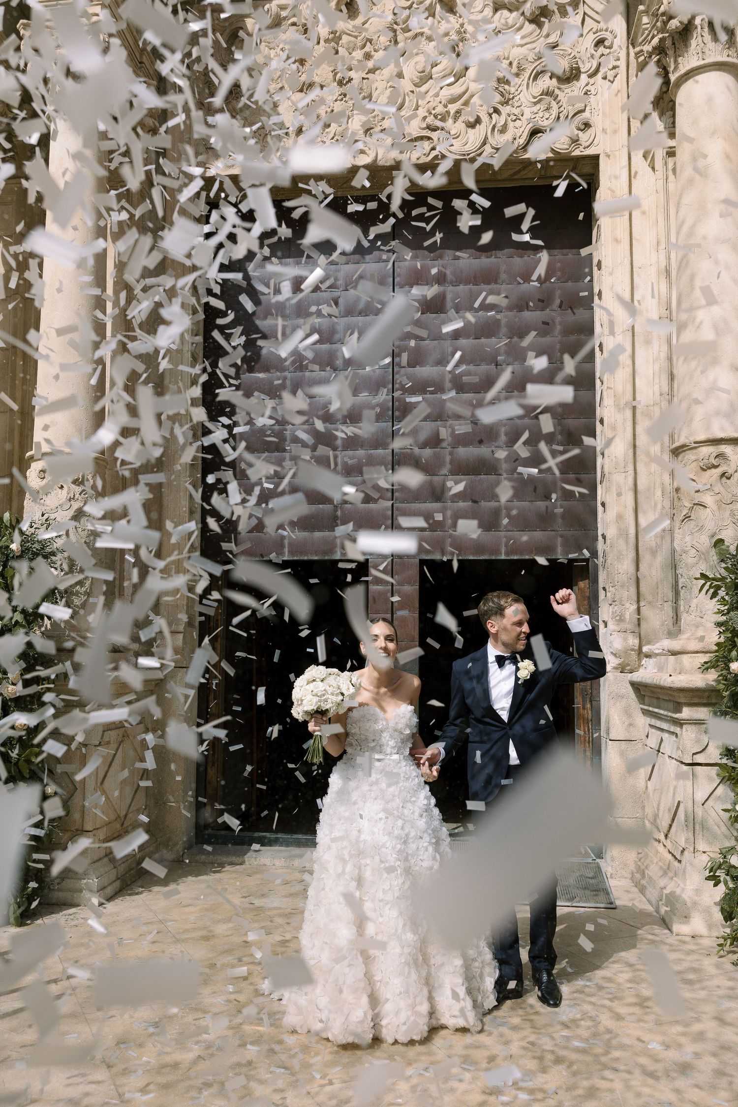 Newlyweds exit church doors under a shower of white confetti petals.
