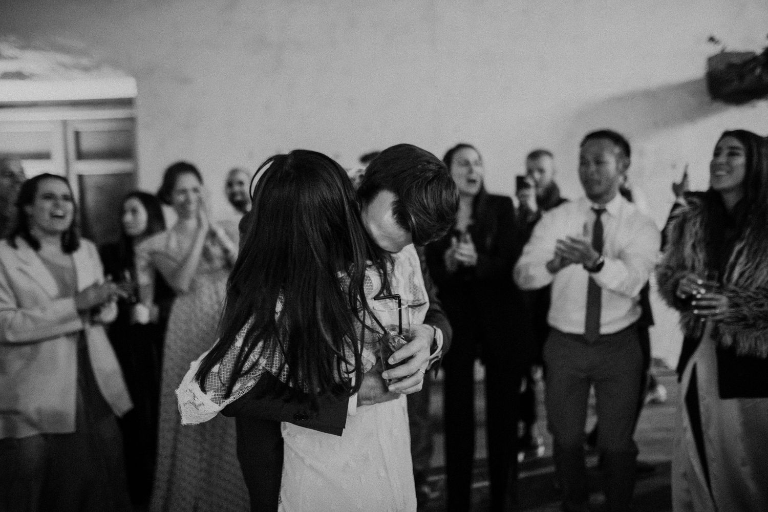 Black and white photo of wedding celebration with guests dancing and socializing indoors.