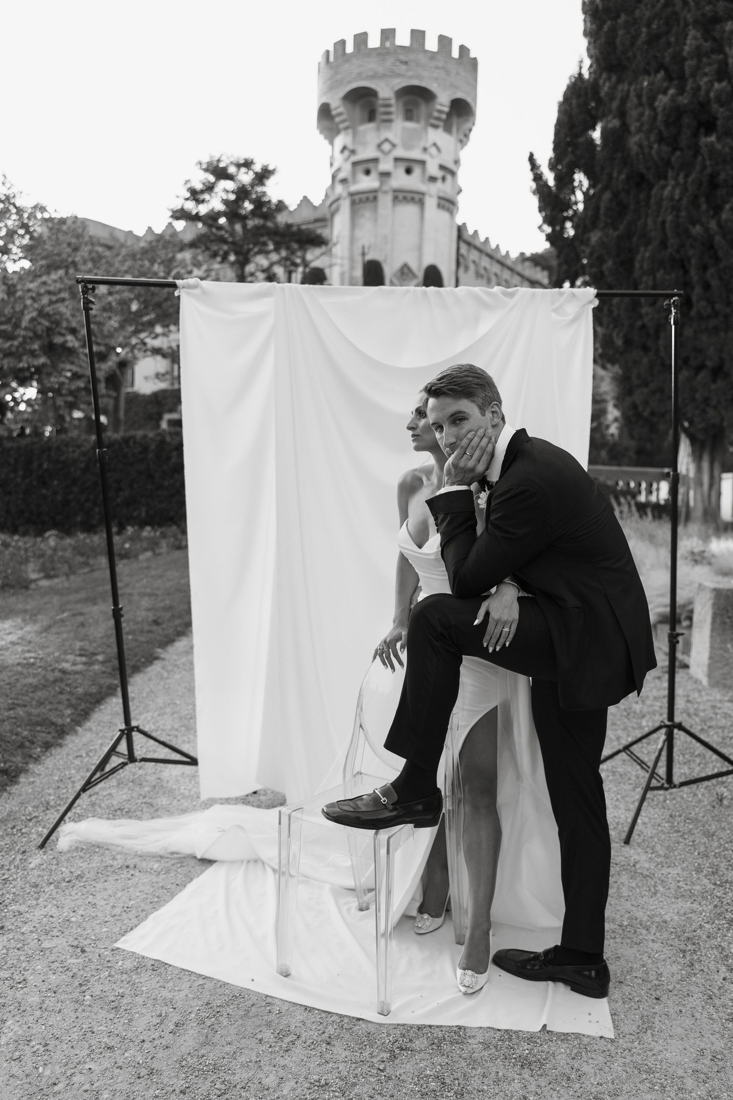 Black and white wedding photo with artistic pose against white backdrop and castle tower.