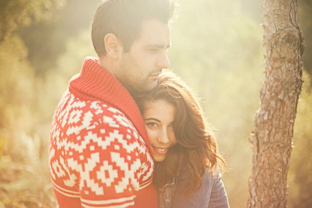 Couple sharing a tender moment in golden sunlight wearing winter sweaters.