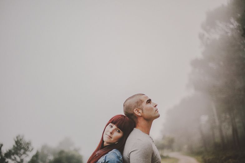 A couple standing close together in a misty outdoor setting.