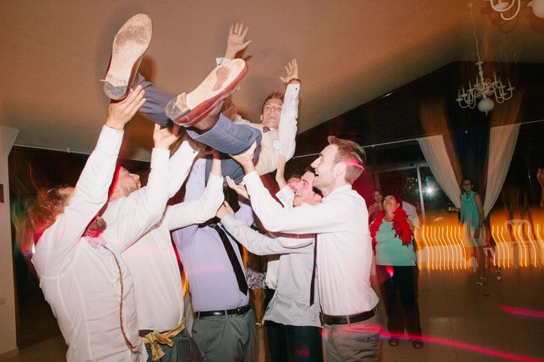 Wedding guests lifting and tossing someone up in the air during a lively dance party celebration.