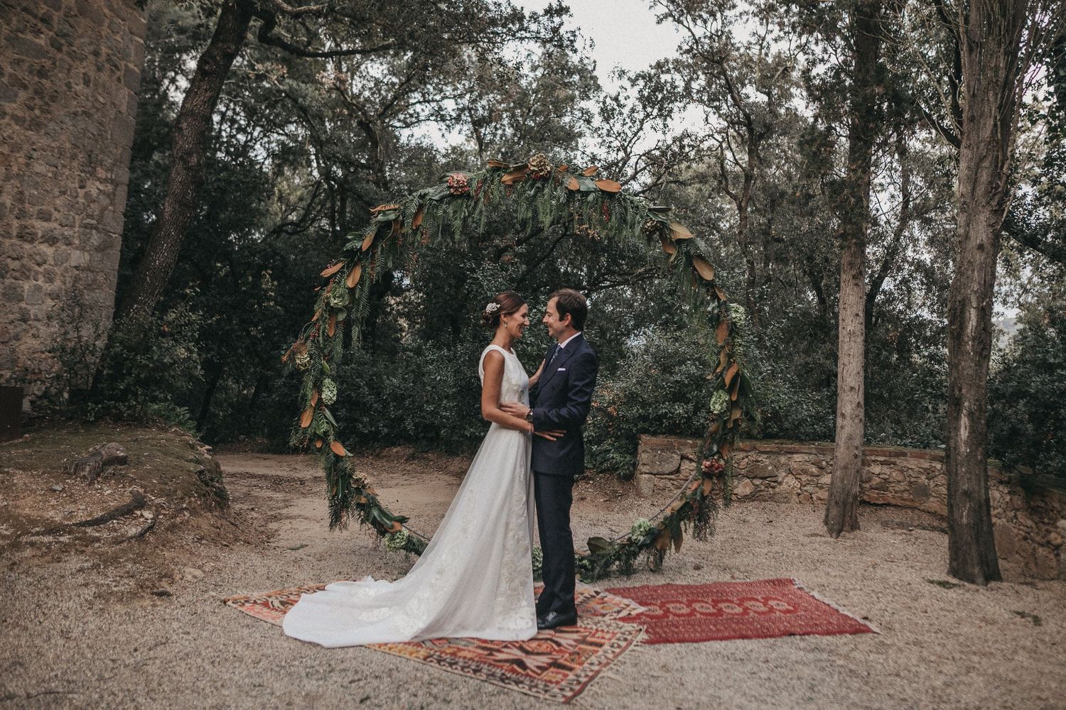 Wedding ceremony setup with a floral arch in a rustic outdoor setting with a red carpet.