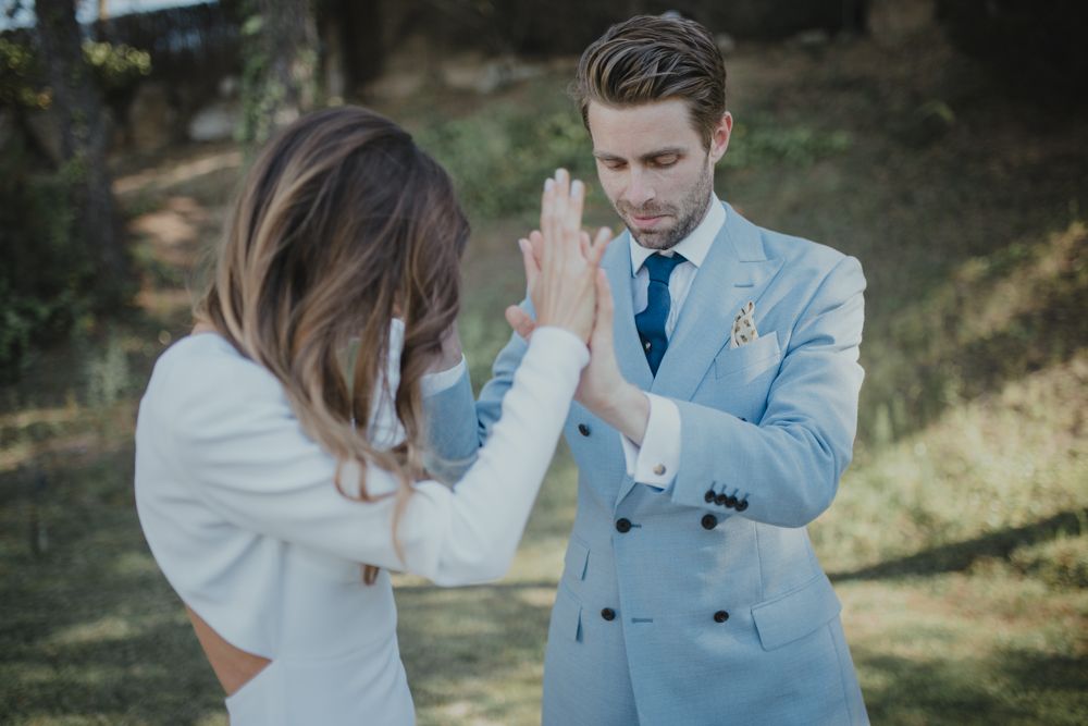 Two people in formal attire sharing a playful high five moment during a wedding photoshoot outdoors.