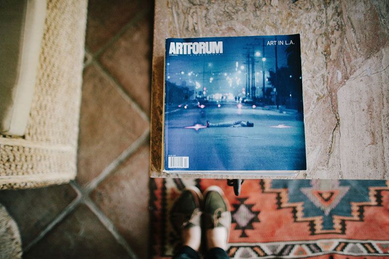 Artforum magazine cover displayed on patterned rug with blue nighttime cityscape.