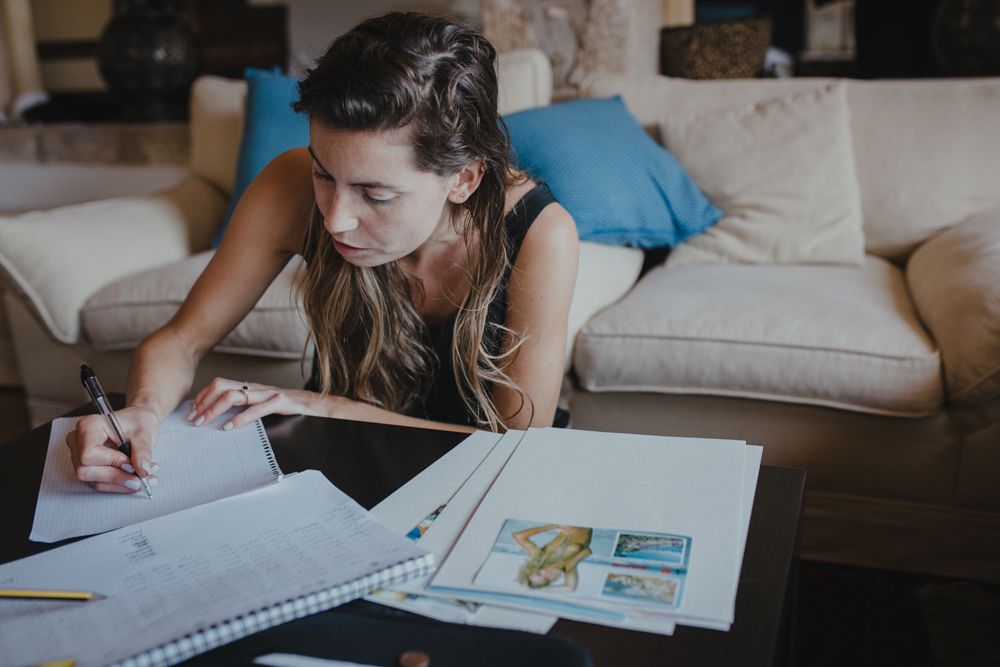 Person lying on couch taking notes while studying documents.