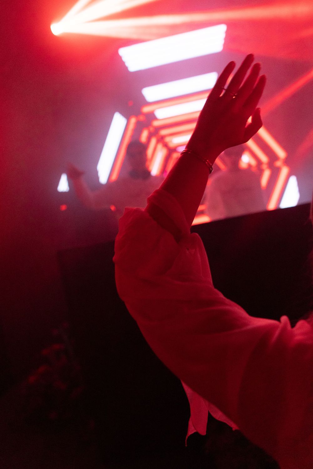 A silhouetted hand raised in a red-lit concert or club environment.