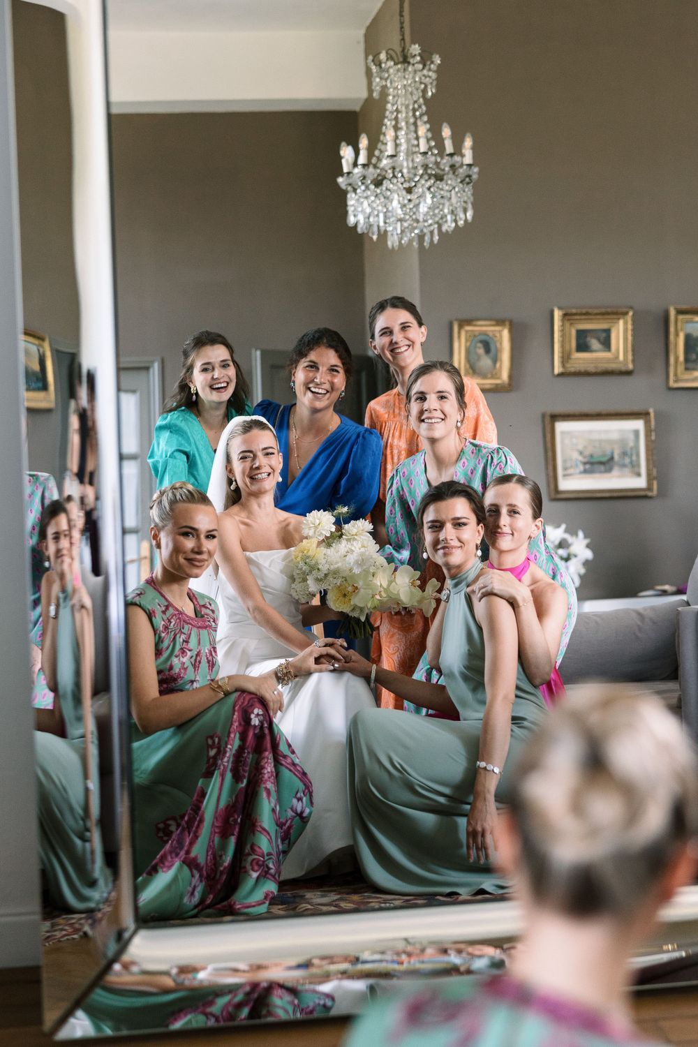 Wedding party members gathered in elegant room with chandeliers and mirrors.