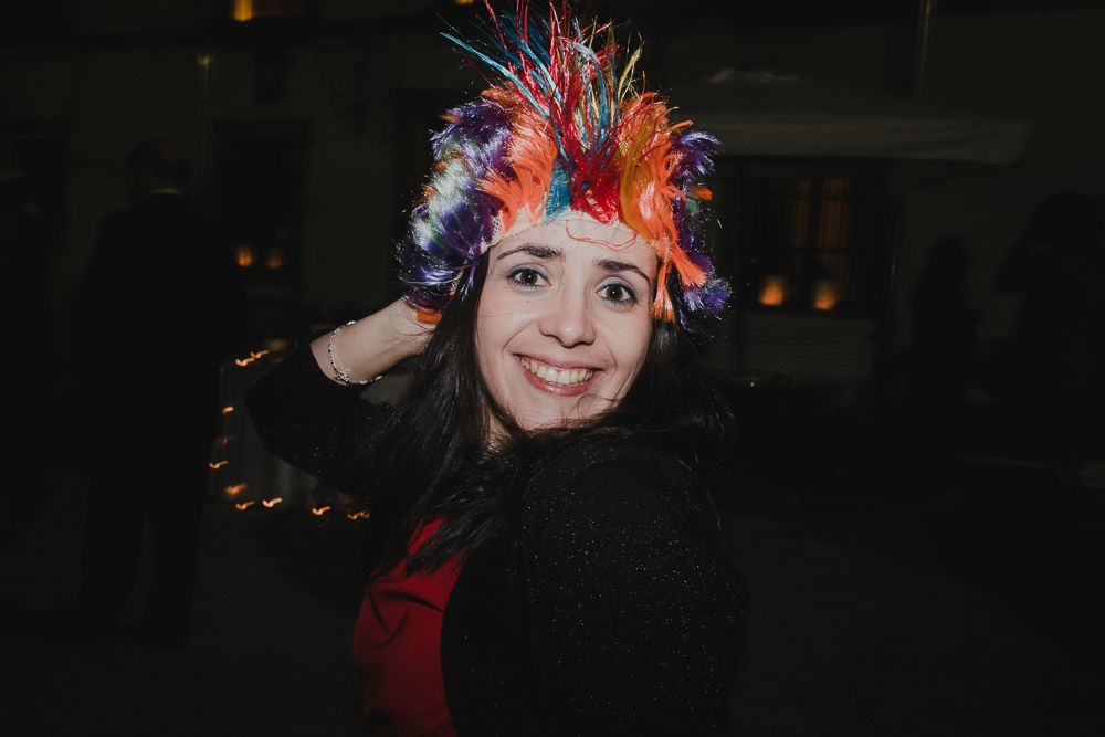 Party guest wearing a vibrant feathered headpiece with bright orange and blue plumes.