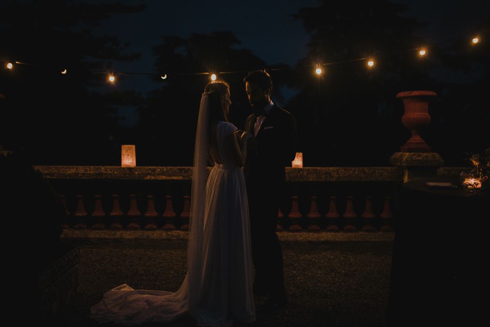 A couple shares an intimate moment on a balcony with string lights in the background.