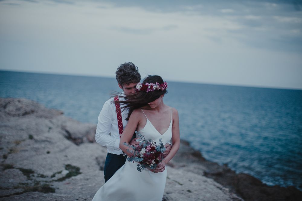 A couple embraces on rocky coastal cliffs during their wedding photoshoot.
