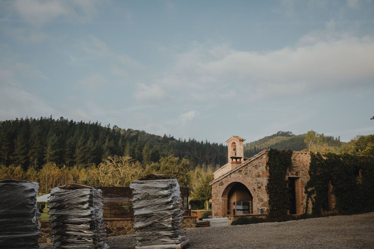 Stone archway entrance with stacks of chairs against forested hillside landscape.