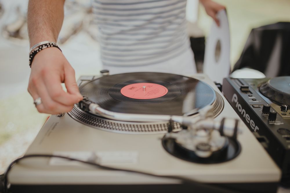 Close-up of hands placing vinyl record on turntable with red label visible.