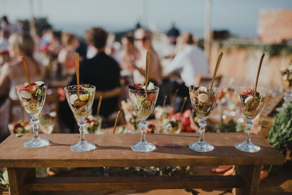 Row of decorated cocktail glasses lined up on wooden table at outdoor event.