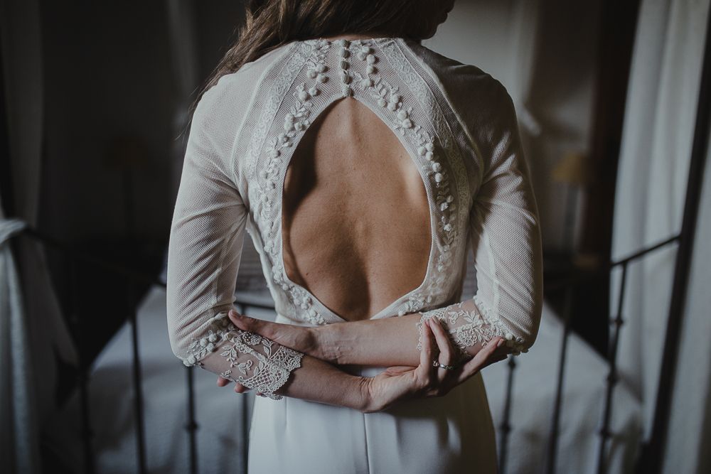 Detailed back of wedding gown featuring delicate buttons and teardrop-shaped open back design.
