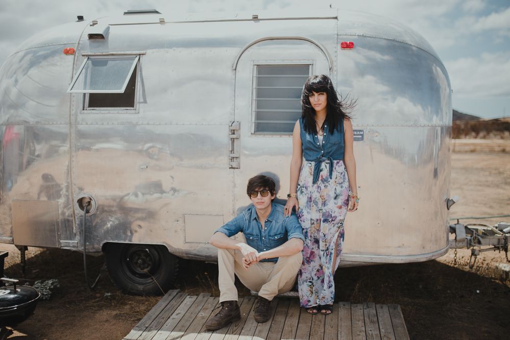 Retro silver Airstream trailer parked in the desert with two people by its entrance.