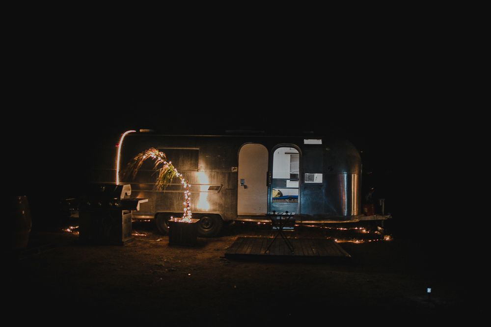 An Airstream trailer illuminated at night with warm lighting creating a cozy outdoor camping scene.