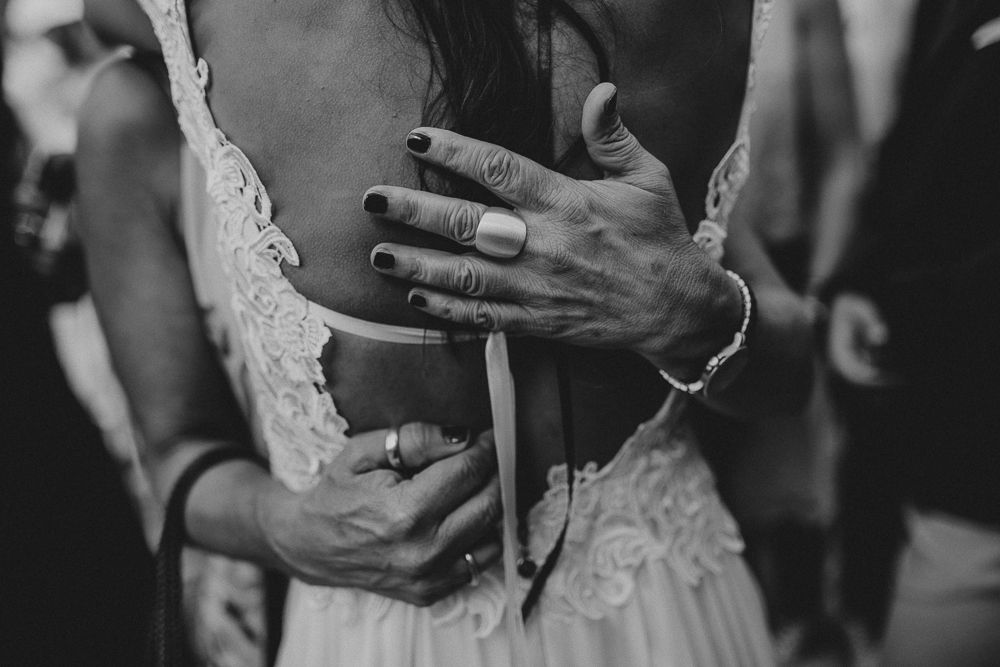Close-up black and white photo of hands embracing on a lace wedding dress.