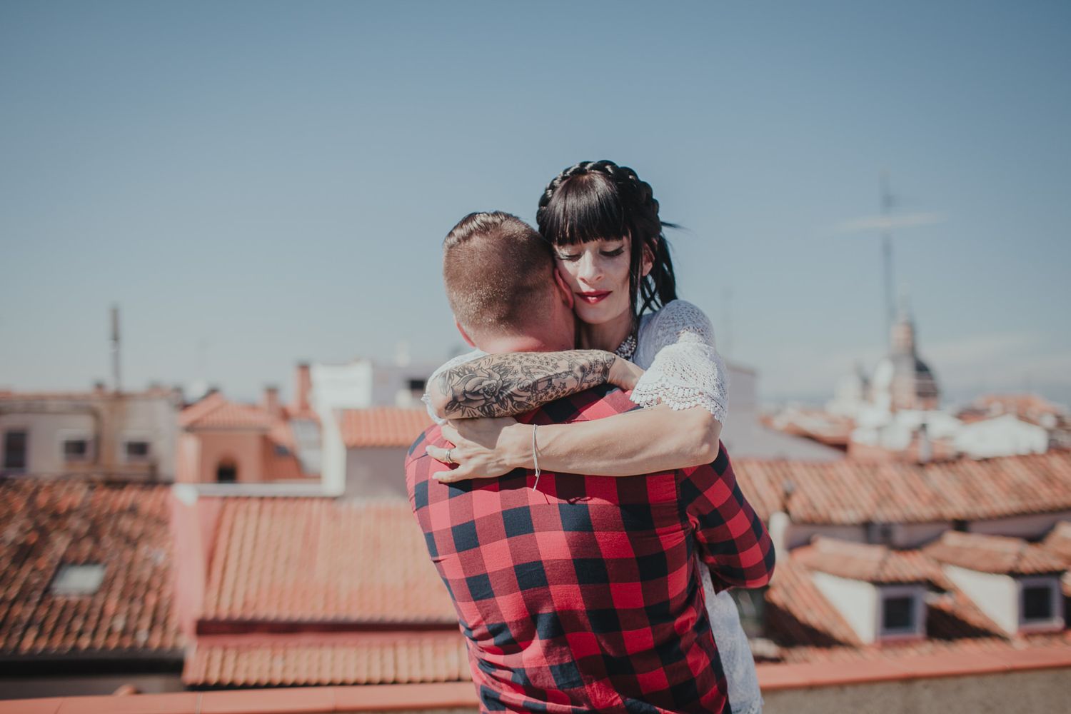 A romantic embrace on a rooftop overlooking terracotta tiles and church spires against a blue sky.