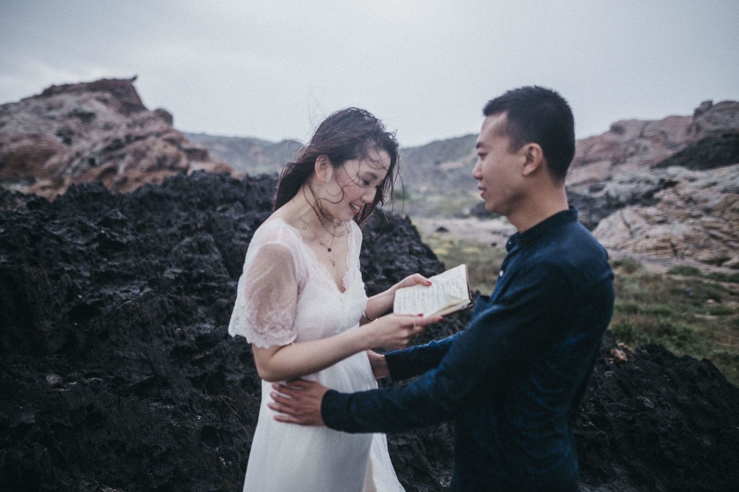 A couple shares an intimate moment while reading together in a rocky outdoor setting.