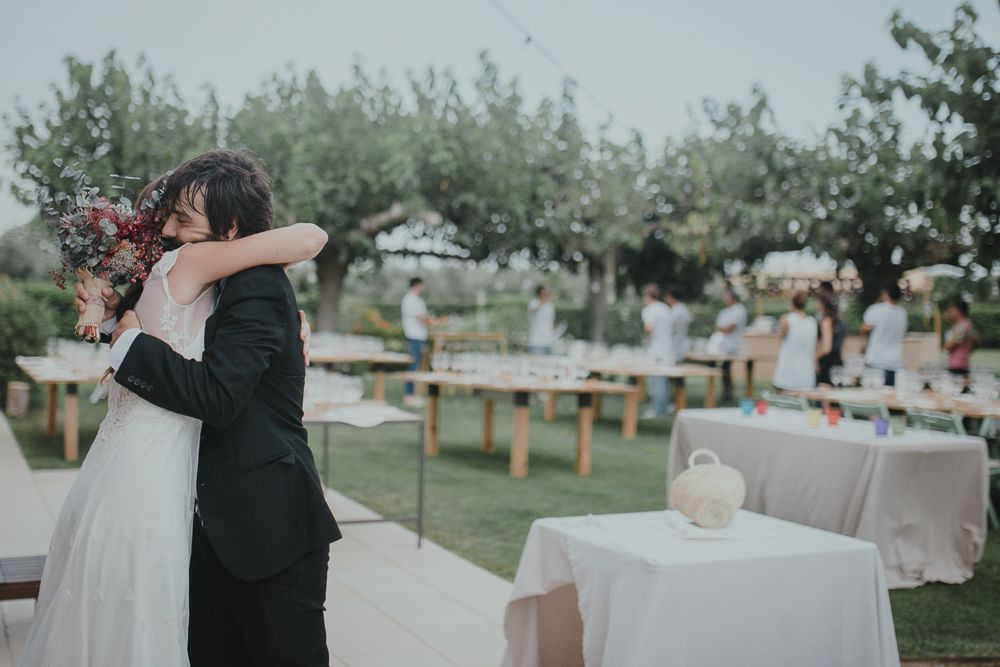 A wedding couple embraces during an outdoor reception with white tables and chairs.