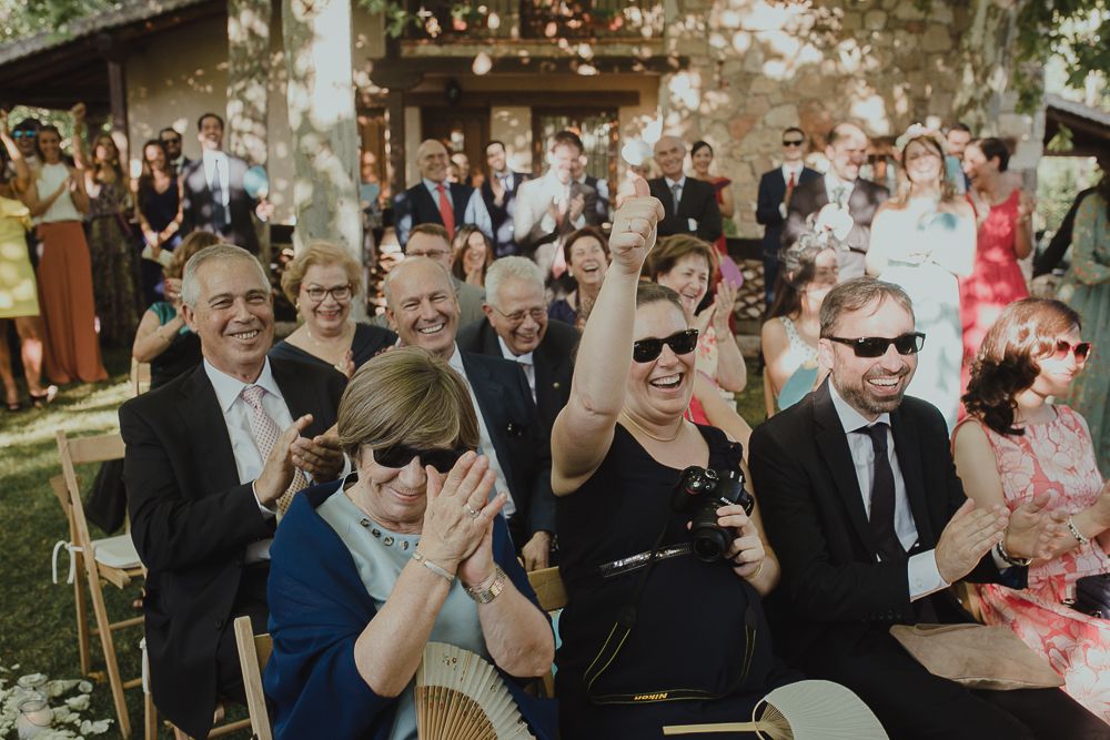 Wedding guests smile and celebrate during outdoor ceremony wearing formal attire.