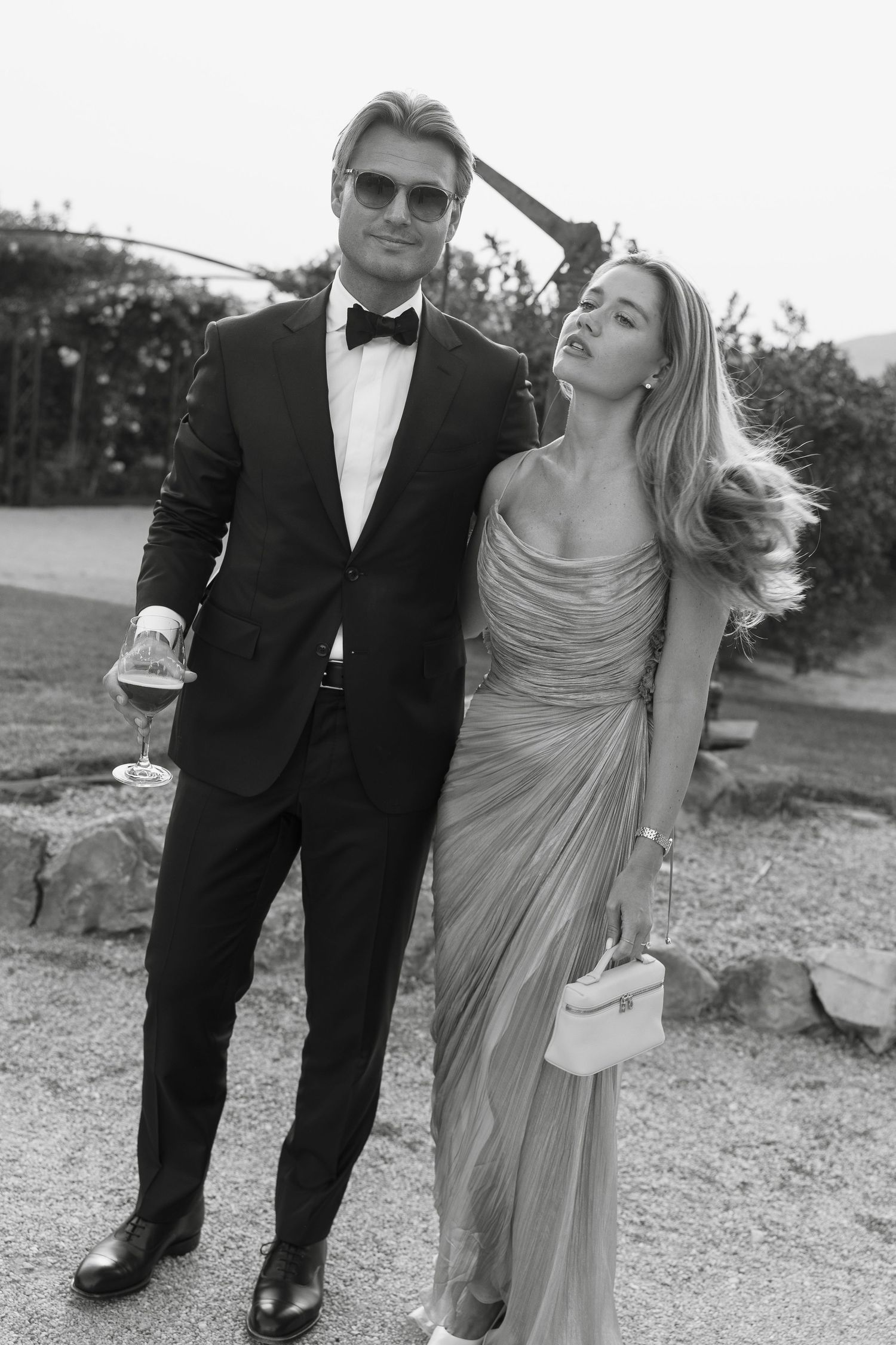 An elegant couple in formal attire poses outdoors at a wedding celebration.