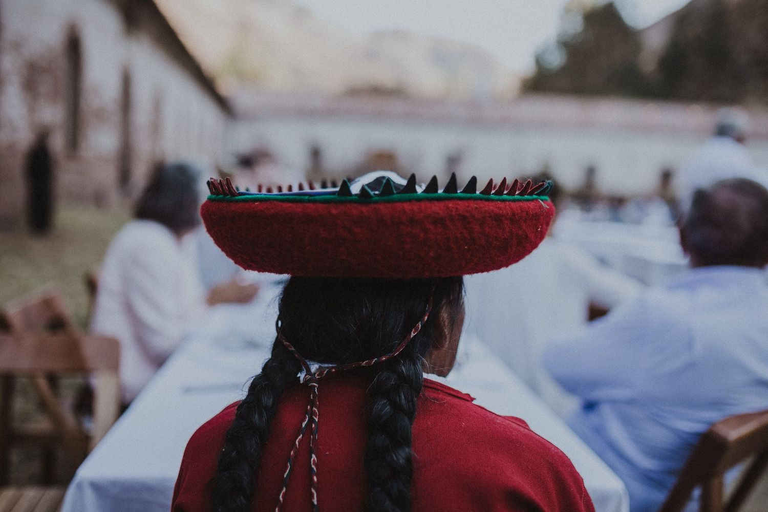 A person wearing a red traditional outfit balancing a decorative basket on their head at an outdoor gathering.