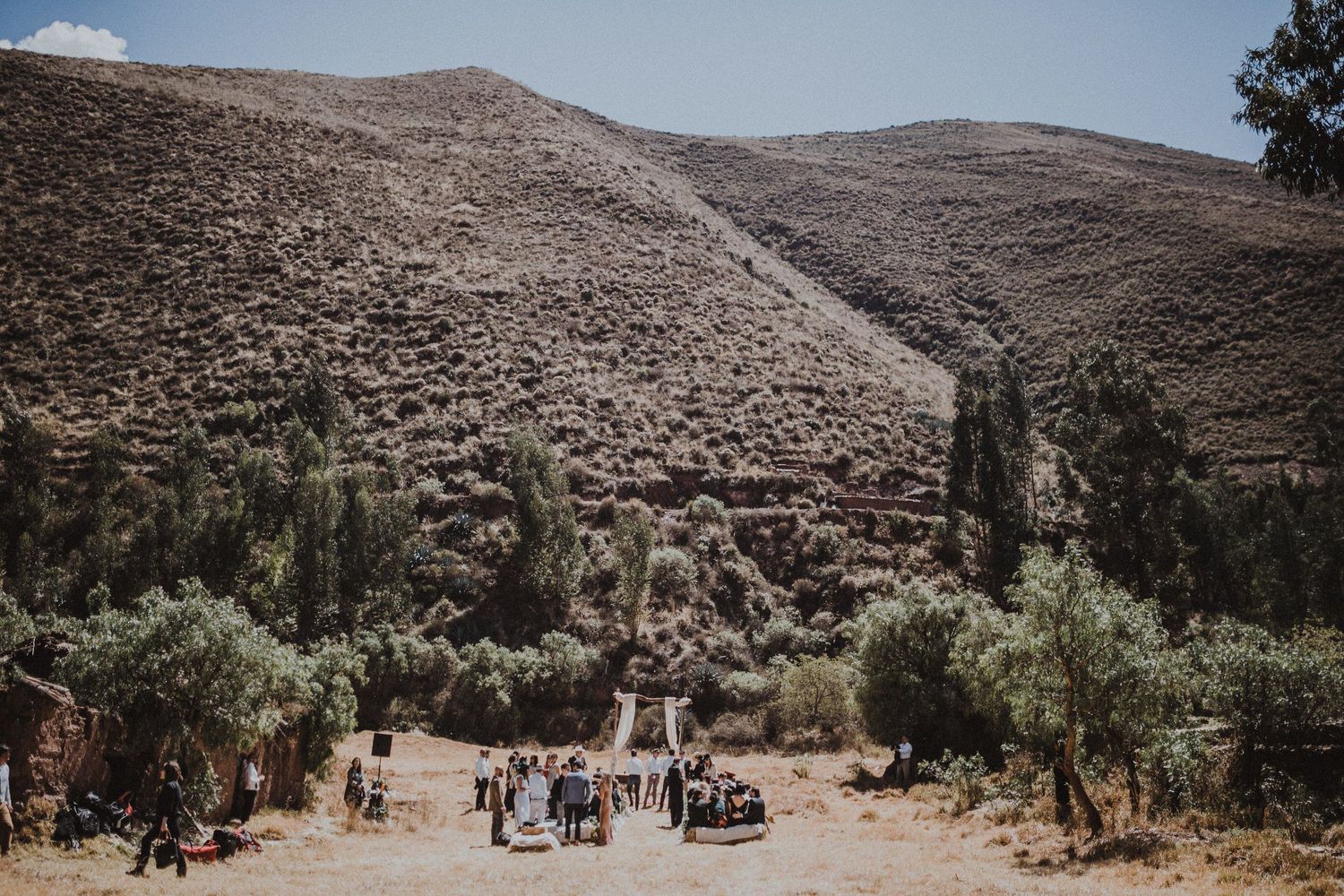Wedding guests gather in a scenic mountain valley surrounded by arid terrain and sparse vegetation.