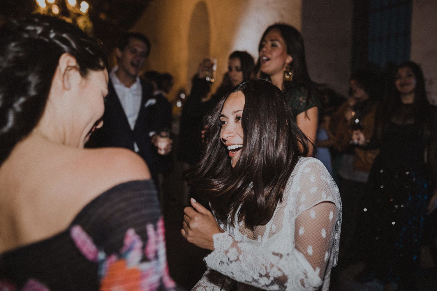 Wedding guests dance enthusiastically at an indoor celebration with arched walls.