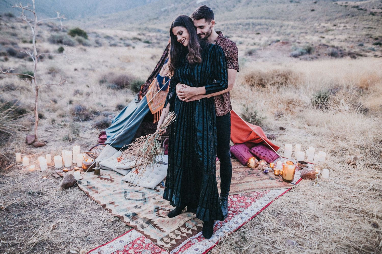 Romantic desert photoshoot with couple standing on colorful rugs among mountains.