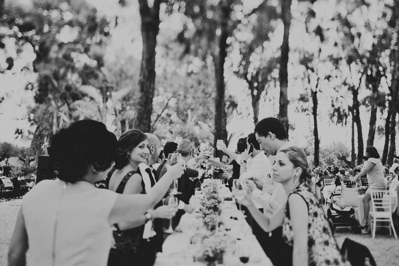 Black and white photo of wedding guests toasting at outdoor reception tables.