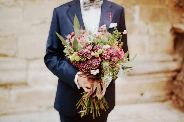 An elegant wedding bouquet with pink and green flowers held against a navy blue suit.