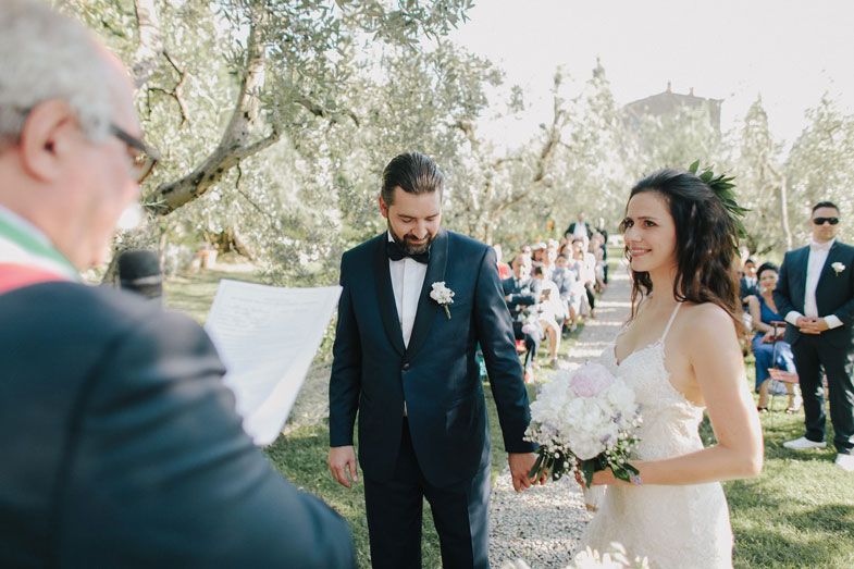 A beautiful outdoor wedding ceremony takes place in a garden setting with guests looking on.