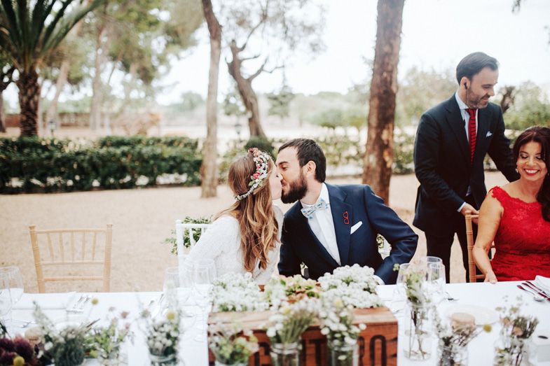 Outdoor wedding reception table decorated with white flowers and greenery under palm trees.