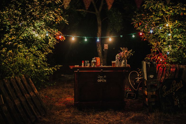 Dark outdoor bar setup with colorful string lights and orange bunting creating a cozy atmosphere.