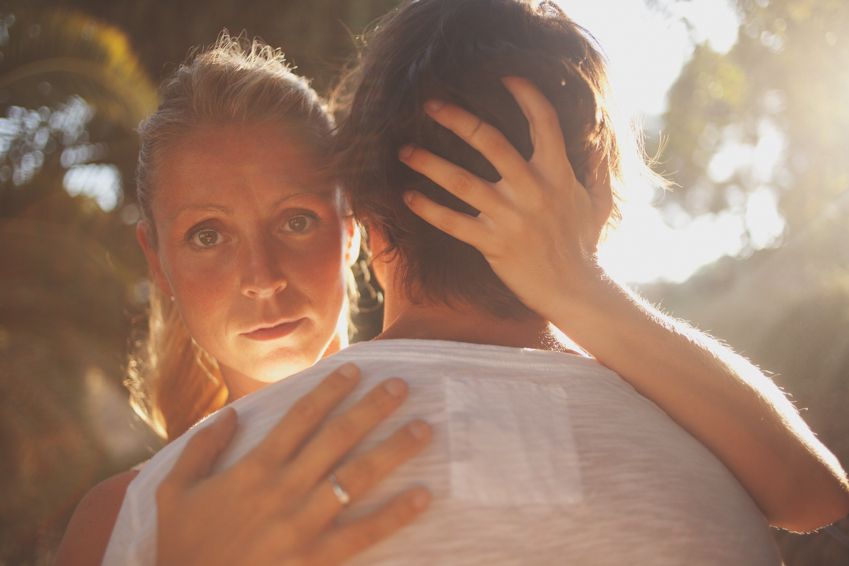 Romantic couple embraces in warm sunlit setting with woman's hand tenderly placed on partner's back.