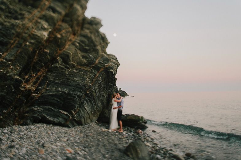 Dramatic coastal wedding photo with cliff face and ocean at sunset.