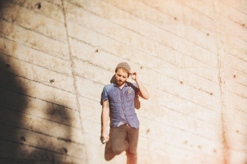 Person in casual attire leaning against a concrete wall in bright sunlight.