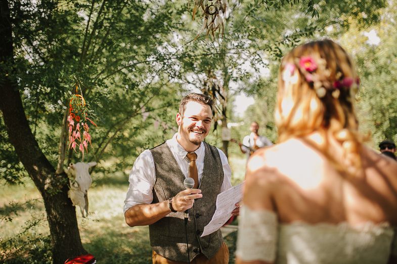 The couple exchanges wedding vows during an outdoor ceremony surrounded by trees and natural lighting.