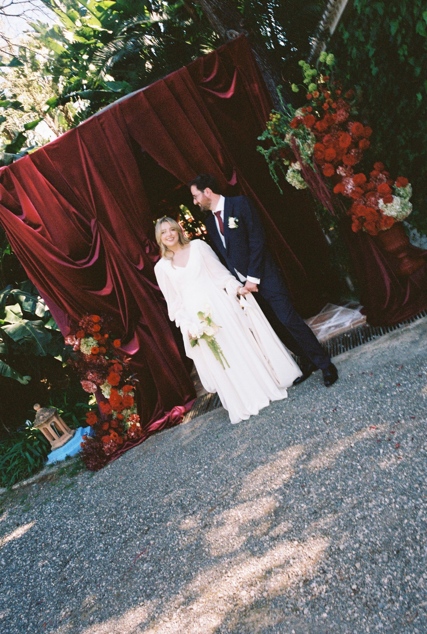 A series of wedding photos showing a couple against a burgundy curtain backdrop with floral arrangements.