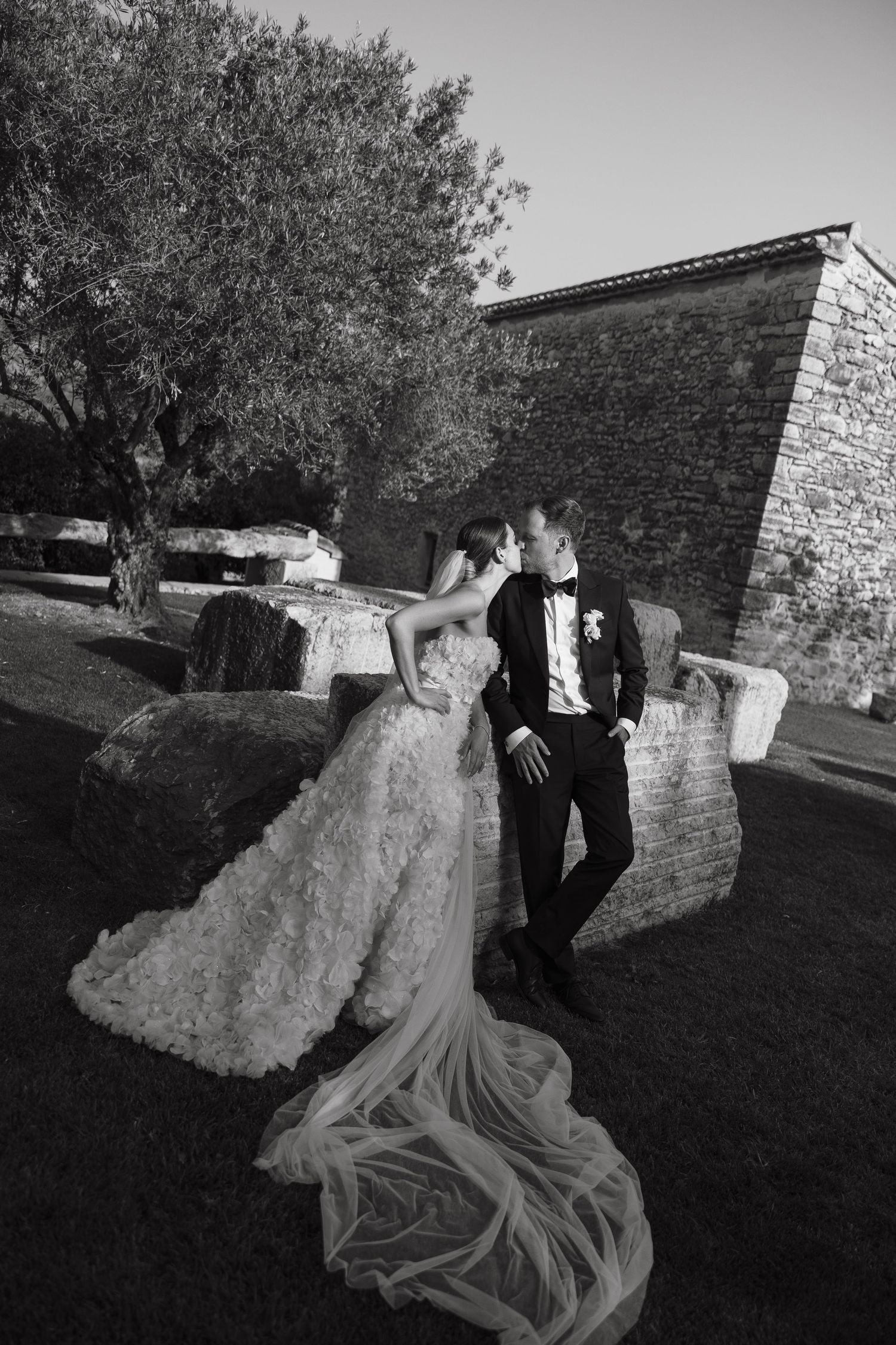 Dramatic black and white wedding portrait by stone wall with flowing bridal gown train.